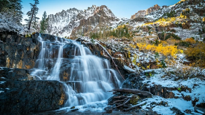 Beautiful Waterfall On Rocks With Landscape View Of Snow And Yellow Flowers Covered Mountains Under Blue Sky 4K 5K HD Nature Wallpaper