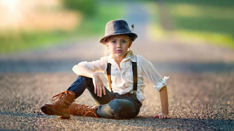 Cute Little Girl Is Sitting On Road Wearing White Blue Dress And Hat In Blur Green Background HD Cute Wallpaper