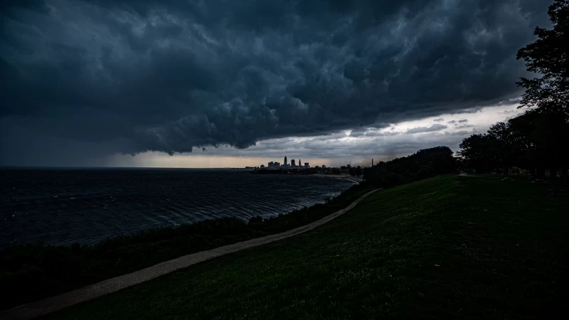 Road Between Green Grass Slope And Ocean Buildings Under Black Clouds White Sky 4K HD Nature Wallpaper