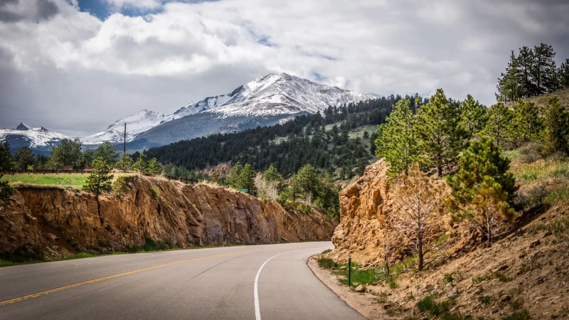 Road Turn Between Rock Trees And Landscape View Of Snow Covered Mountains Under White Clouds Blue Sky 4K HD Nature Wallpaper